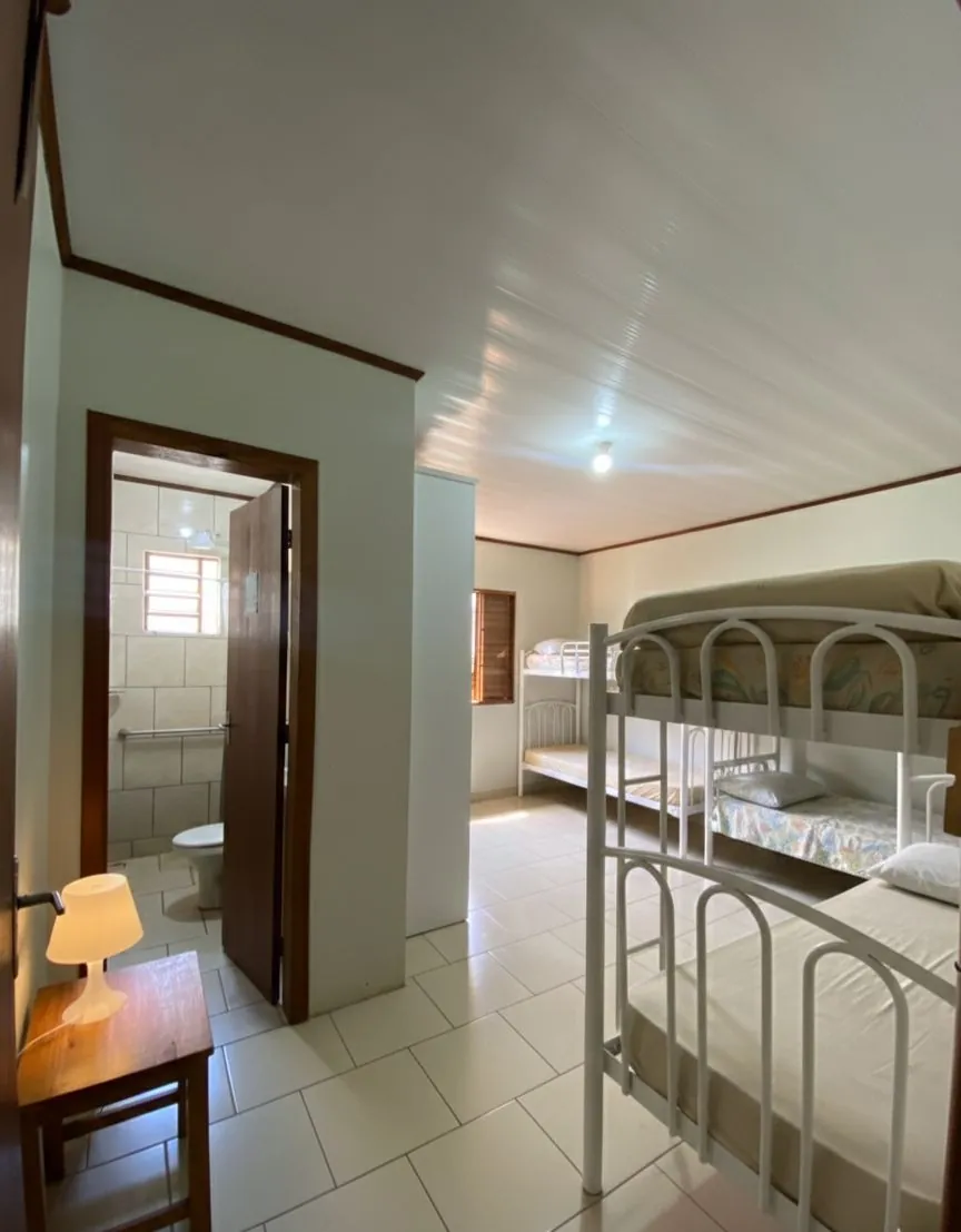 Quarto claro com beliches, luminária e banheiro