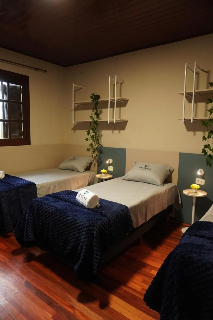 Quarto com duas camas arrumadas, prateleiras e piso de madeira